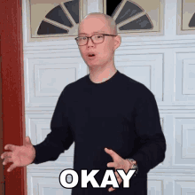 a bald man wearing glasses says okay in front of a white garage door