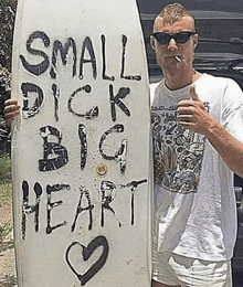 a man holding a surfboard that says small dick big heart on it