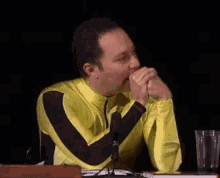 a man in a yellow and black outfit is sitting at a table with his hands folded and smiling .