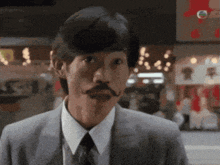a man in a suit and tie with a mustache is looking at the camera .