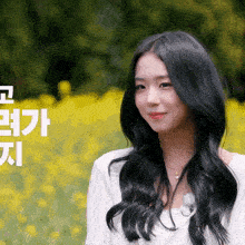 a woman in a white shirt stands in front of a field of yellow flowers with chinese writing behind her