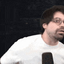 a man wearing glasses and a white t-shirt is talking into a microphone