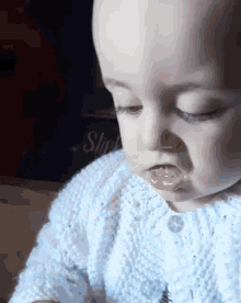 a baby in a white sweater is looking at something with a sign in the background that says slip