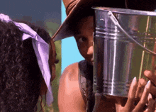 a woman in a cowboy hat is holding a metal bucket