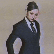 a woman in a black suit and tie is standing with her hands on her hips .