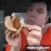 a man in a red shirt is eating a hamburger in a car