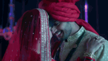 a bride and groom are hugging each other and the bride is wearing a red veil