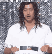 a man with long hair is wearing a white shirt and holding a sign that says ' a ' on it .