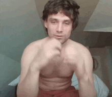 a shirtless man is sitting on a bed making a funny face with his hands .