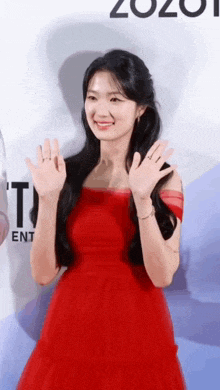 a woman in a red dress is waving her hand and smiling .