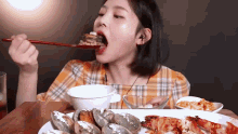 a woman is sitting at a table eating food with chopsticks .