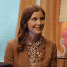 a woman wearing a brown jacket and a brooch smiles for the camera