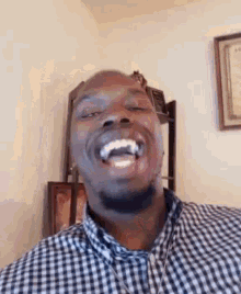 a man in a plaid shirt is laughing with his mouth open in a living room .