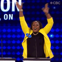 a woman in a yellow jacket is raising her arms in the air while standing in front of a microphone .
