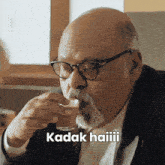 a bald man with glasses and a beard drinks from a glass with the words kadak haiiii written below him
