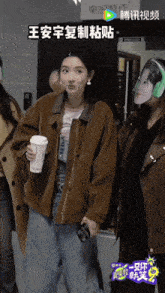 a woman in a brown jacket is holding a coffee cup