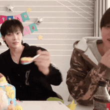 a man is eating cake with a spoon while another man watches
