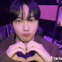 a man is making a heart shape with his hands while sitting in a chair .