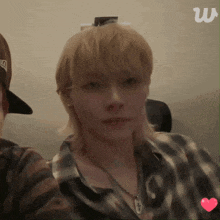 a man with blonde hair is wearing a plaid shirt and a hat with the letter w on it