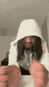 a man with dreadlocks wearing a white hoodie is sitting at a table .