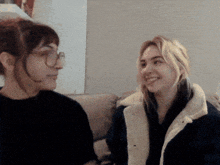 a woman wearing glasses and a white jacket smiles at another woman