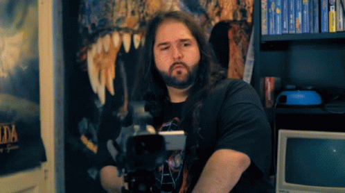 a man with long hair and a beard stands in front of a wall with a poster that says zelda