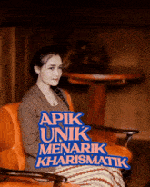 a woman sits in an orange chair with a sign that says apik unik menarik kharismatik