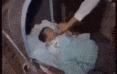 a baby is laying in a crib with a person holding its hand .