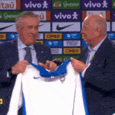 a man in a suit is holding a blue and white nike jersey