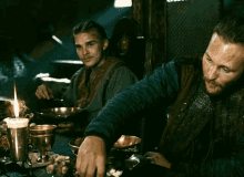 two men sitting at a table with candles and bowls of food