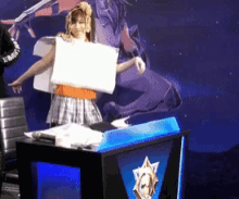a woman holding a piece of paper in front of a podium that says ' league of legends ' on it