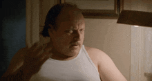 a man with a mustache wearing a white tank top is standing in front of a lamp