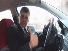 a man in a suit and tie is giving a thumbs up while sitting in a car