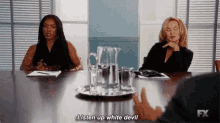 two women are sitting at a table with a pitcher of water and glasses .