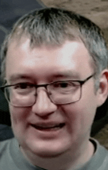 a man wearing glasses and a grey shirt is smiling .