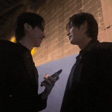 two men are standing next to each other one is holding a cell phone