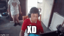 a boy wearing headphones is sitting in front of a computer with the text xd on the screen