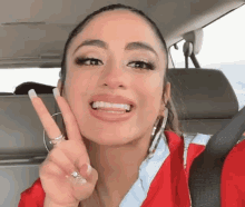 a woman in a red jacket is giving the peace sign