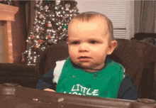 a baby is wearing a green bib that says little