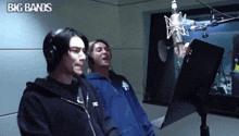two men singing into microphones with big bands written above them