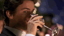 a man in a tuxedo is drinking from a glass .