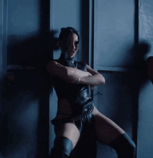 a woman in a black leather outfit is standing in a dark room with her arms crossed