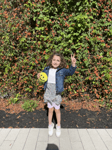 a little girl in a denim jacket holds a yellow smiley face