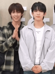 two young men are standing next to each other with their hands folded in front of them .