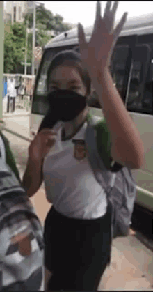 a woman wearing a mask and a backpack is waving at a bus .