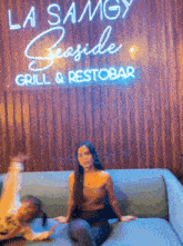 a woman is sitting on a couch in front of a sign for la sangy seaside grill & restobar