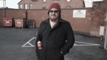 a man wearing a red hat and sunglasses is standing in a parking lot with a sign that says car park