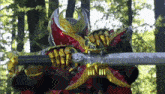 a person in a red and gold costume is holding a large sword in a forest .