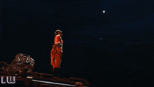 a woman in a red dress stands on top of a truck in front of a large red eye with the letters luw below it