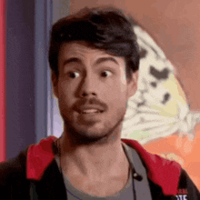 a man with a beard is wearing a red jacket and making a funny face .